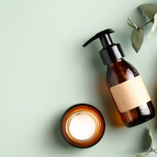 Natural organic SPA cosmetic products set with eucalyptus leaves. Top view herbal skincare beauty products on green background. Amber glass dispenser, spray bottles, jar of moisturizer cream.